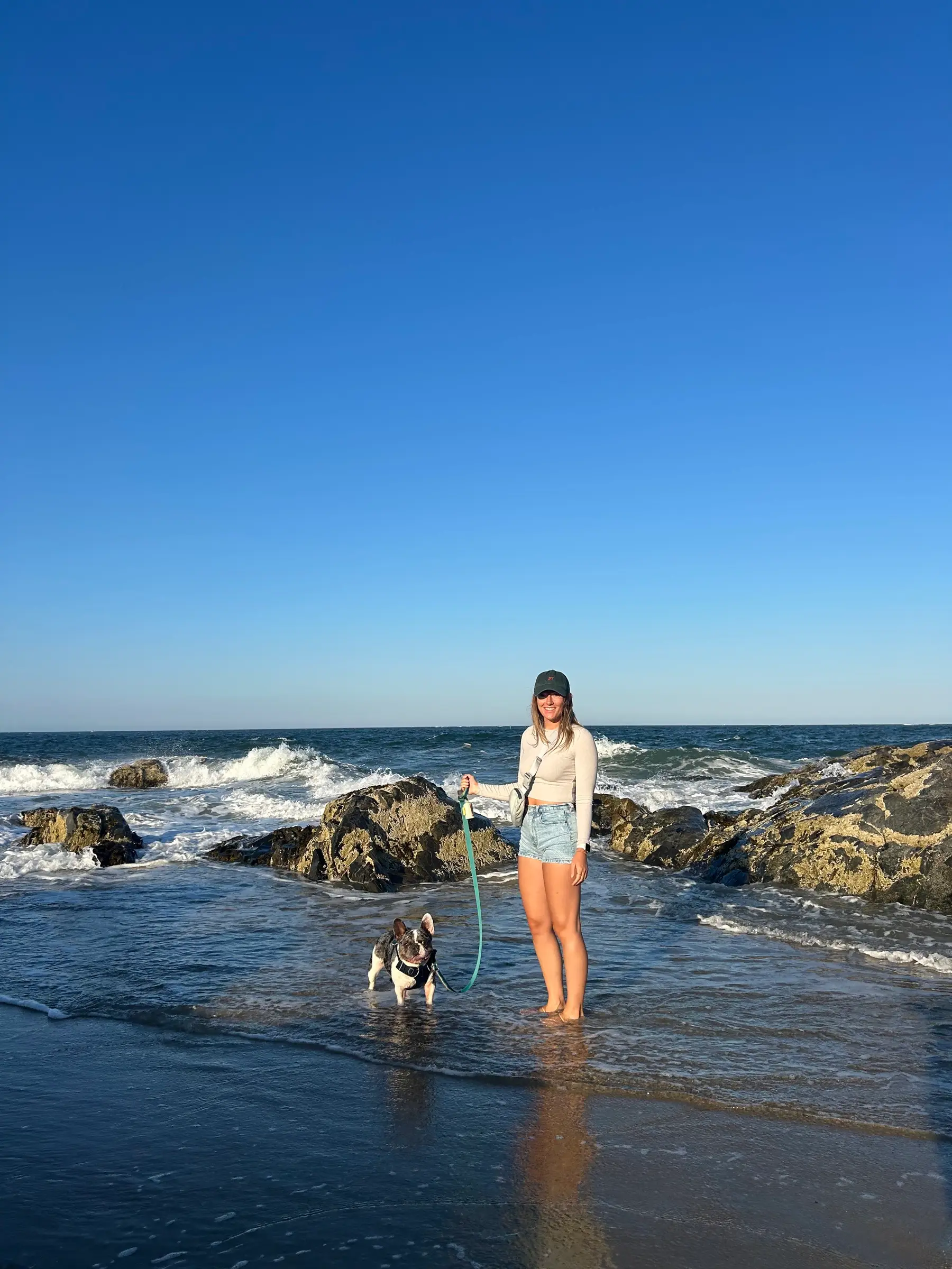 Sally holding Louie, her French bulldog, on a rocky New England beach at golden hour